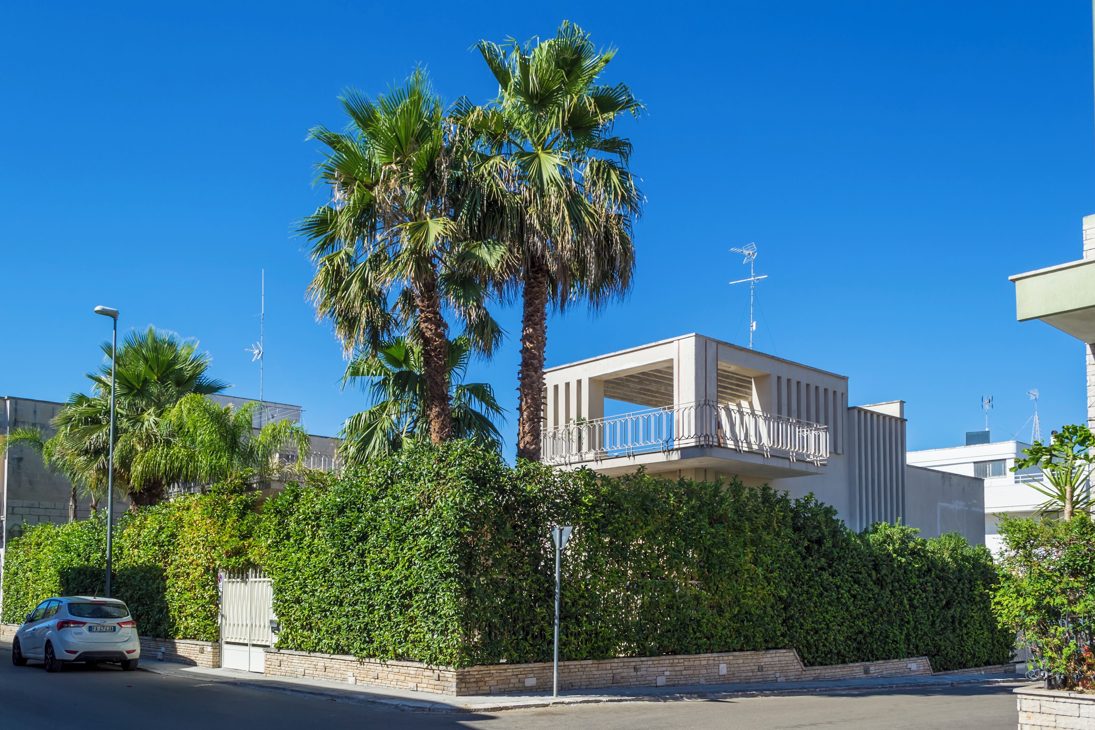 Un edificio moderno con balcón, rodeado de vegetación exuberante y palmeras.