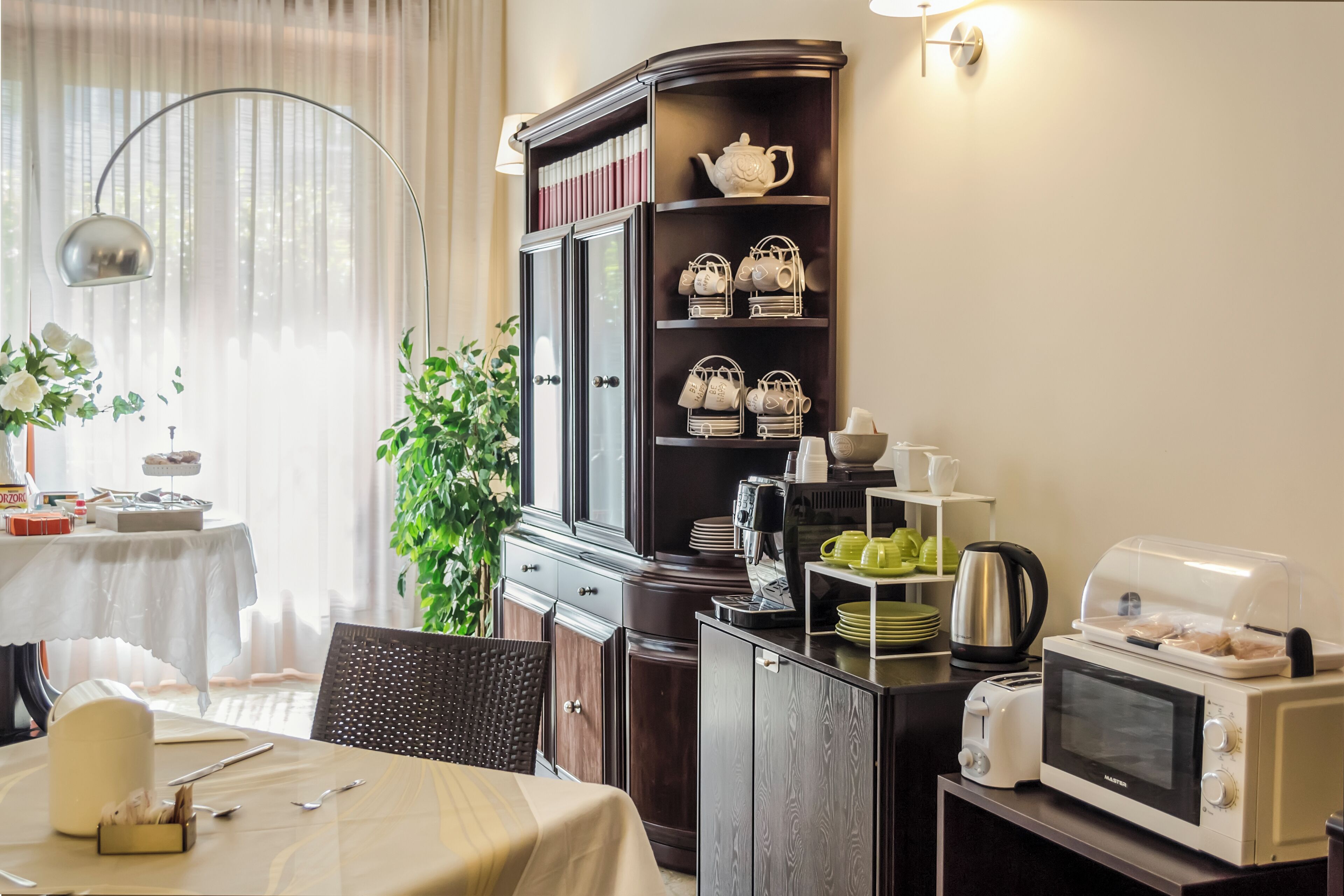 Un comedor con una mesa dispuesta para dos, un armario con utensilios de cocina, un microondas y un tostador.