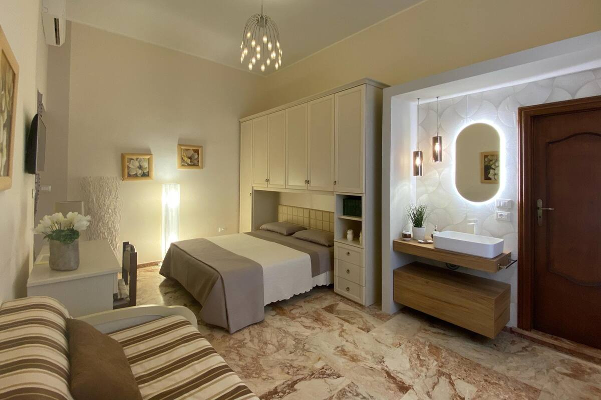 Une chambre à coucher comprenant un lit, une table de chevet, une lampe et un miroir doté d’un éclairage intégré.