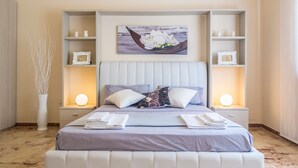 Een netjes ingerichte slaapkamer met een groot bed, twee nachtkastjes met lampen, een decoratieve vaas en een ingelijst schilderij aan de muur.