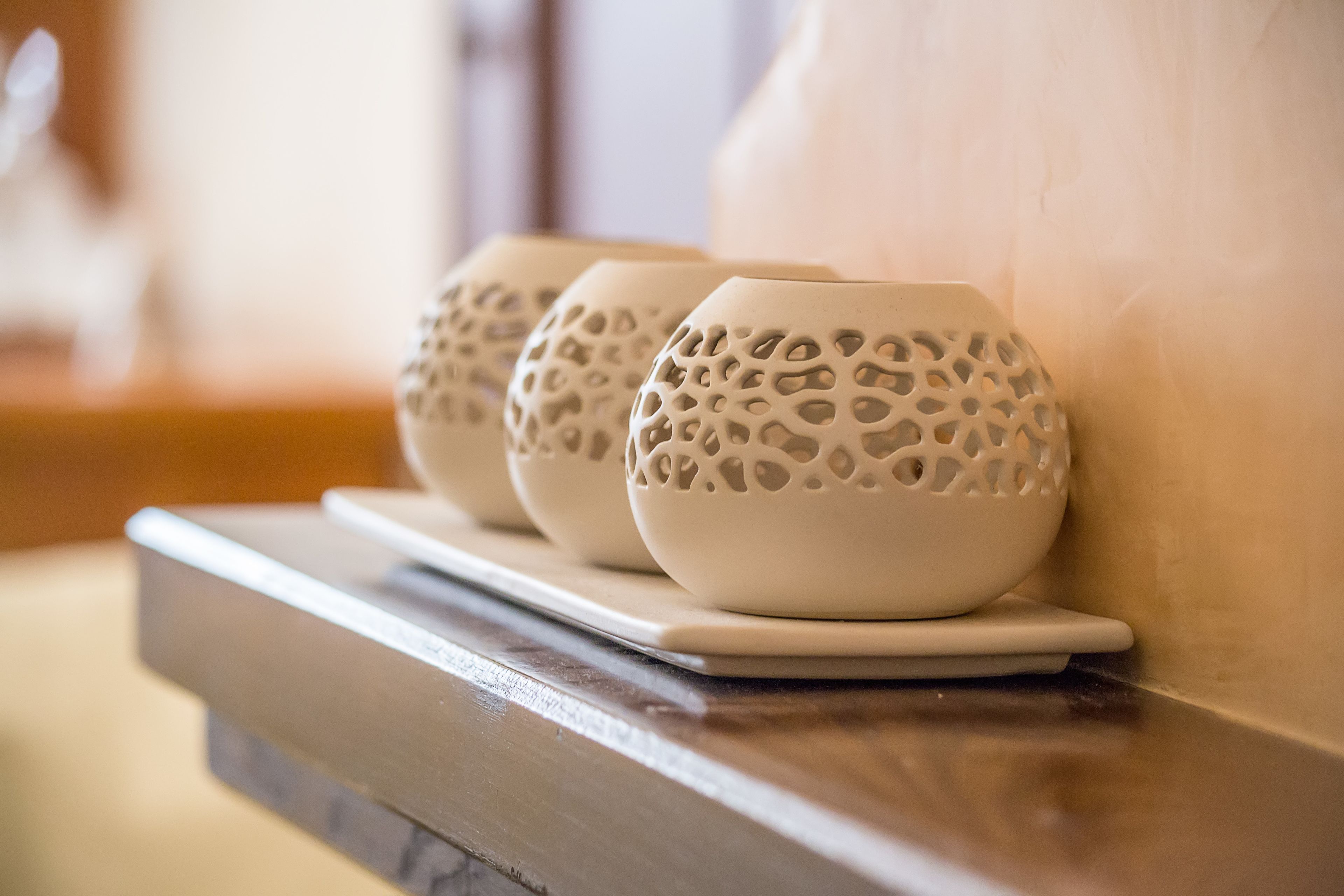 Three white ceramic bowls with perforated patterns on a white tray, placed on a wooden ledge against a wall.