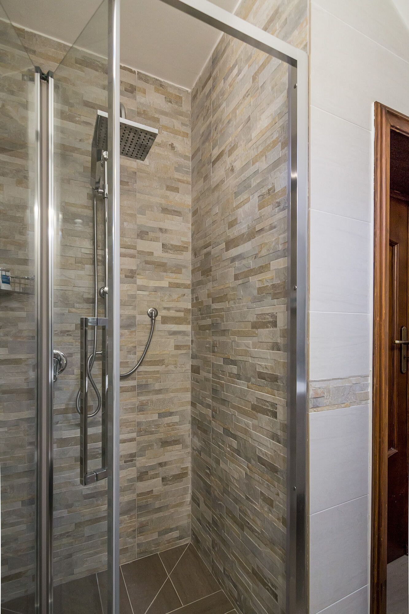 Une douche entièrementClose avec des parois en verre, un mur imitant la pierre et une porte en bois.