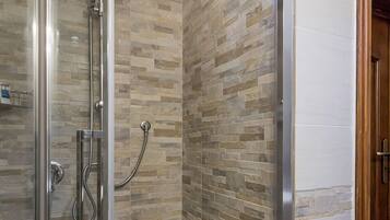 Une douche entièrementClose avec des parois en verre, un mur imitant la pierre et une porte en bois.