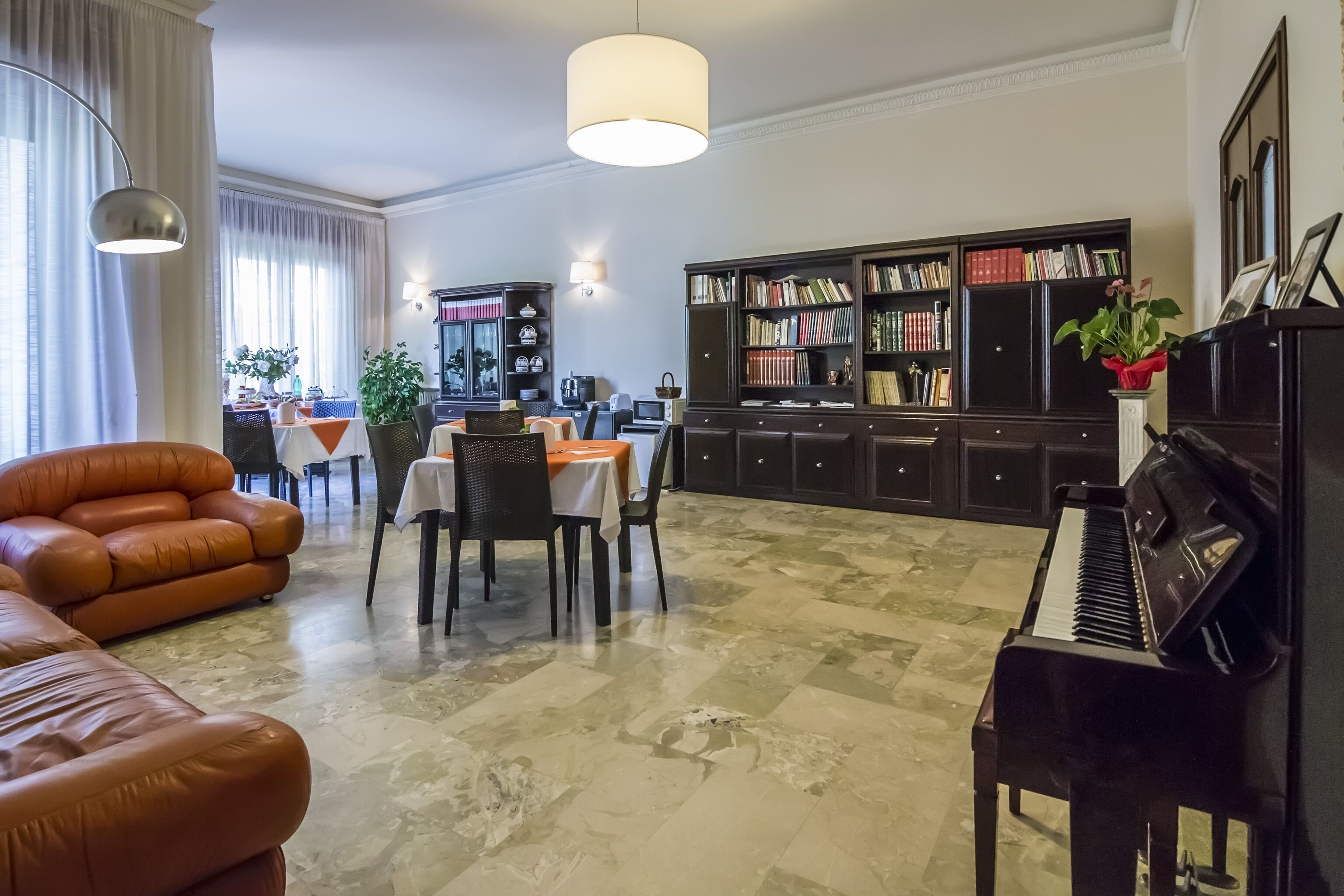 A spacious living room with a piano, leather sofa, dining area, and a large bookshelf.