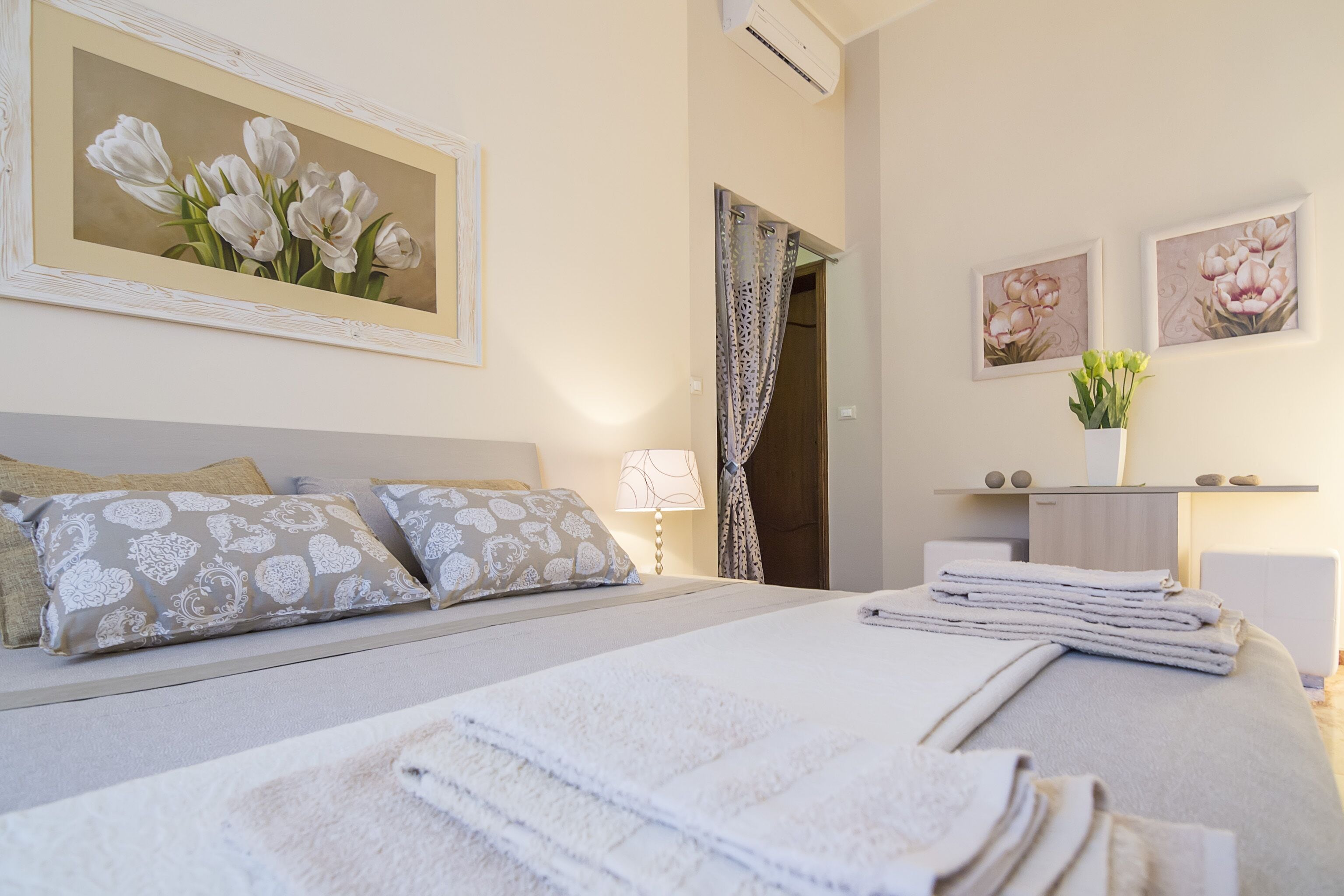 A neatly made bed with pillows, a bedside lamp, and a framed painting of flowers on the wall.