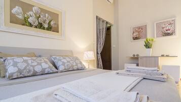 A neatly made bed with pillows, a bedside lamp, and a framed painting of flowers on the wall.