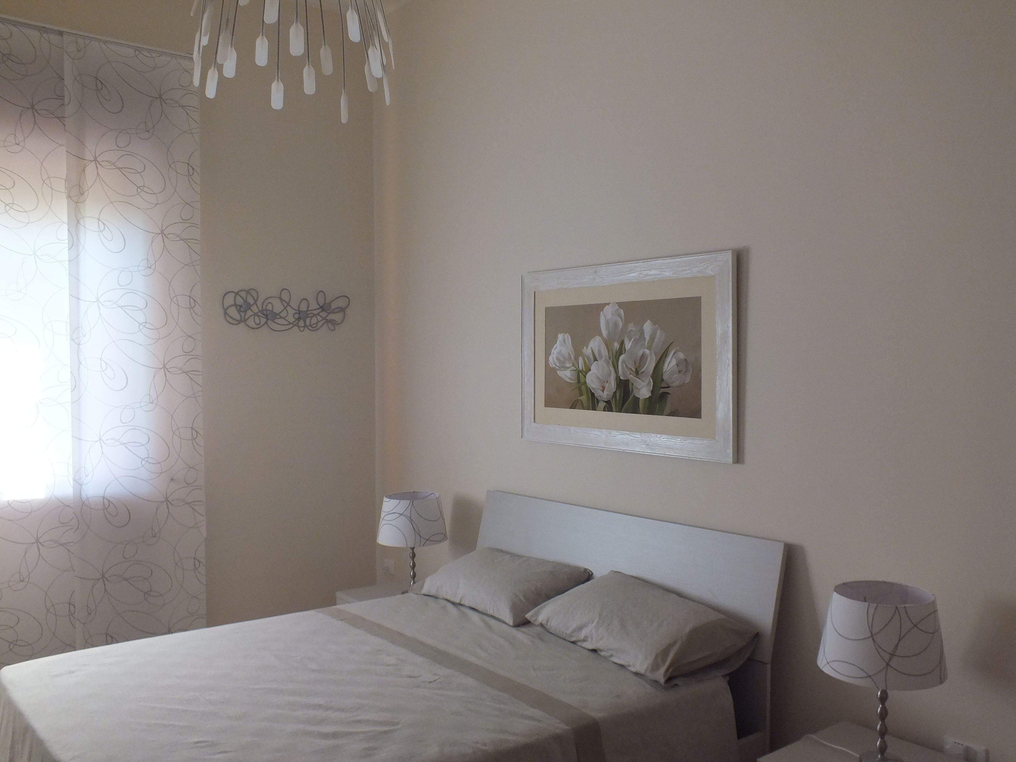 Ein Schlafzimmer mit einem Bett, zwei Nachttischlampen, einem gerahmten Blumenbild und einem Wanddekor.