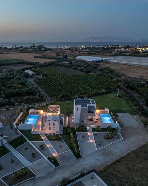 A modern villa with two swimming pools, surrounded by landscaped gardens and vineyards.