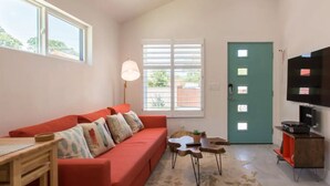 Una sala de estar con un sofá rojo, una mesa de madera, un ventilador de techo y una puerta color turquesa.
