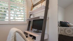 Un dormitorio con una cama, un escritorio con computadora y una ventana con persianas.