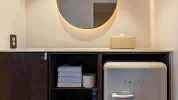 A compact kitchenette with a white refrigerator, a built-in oven, a mirror, and a shelf with towels and a basket.