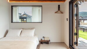 A bedroom with a large bed, a small bedside table, a window with a view of traditional architecture, and a wooden ceiling. - Hwarangroo (Gyeongju)