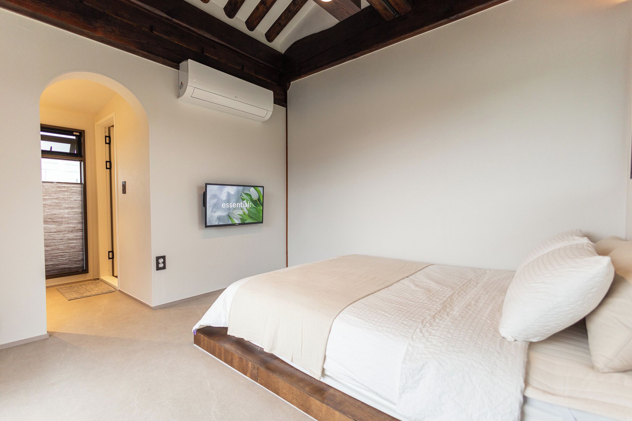 A bedroom with a bed, a TV mounted on the wall, and an arched doorway leading to another room.