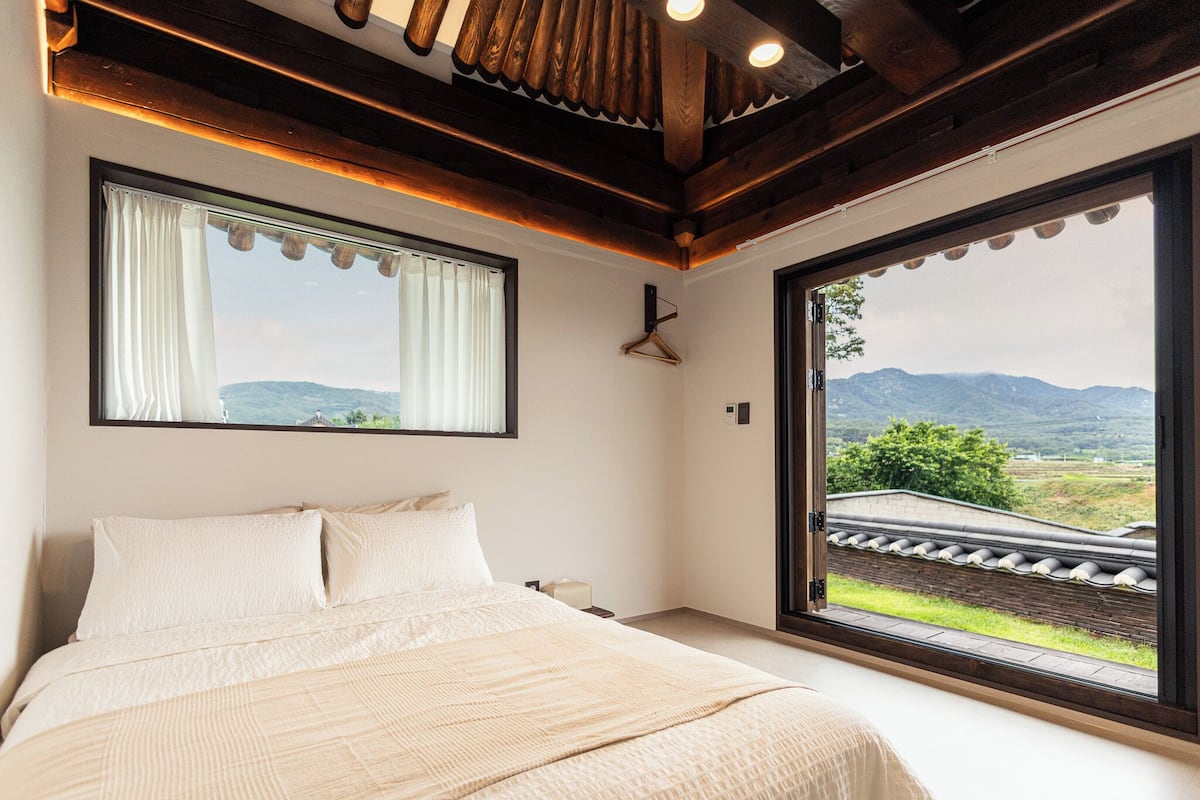 A bedroom with a large bed, a window with curtains, and a view of mountains.
