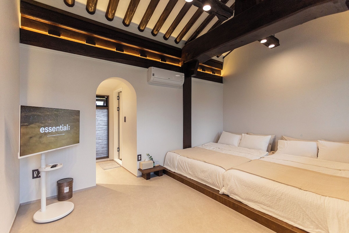 A modern hotel room with a large bed, a flat-screen TV, and a wooden ceiling.
