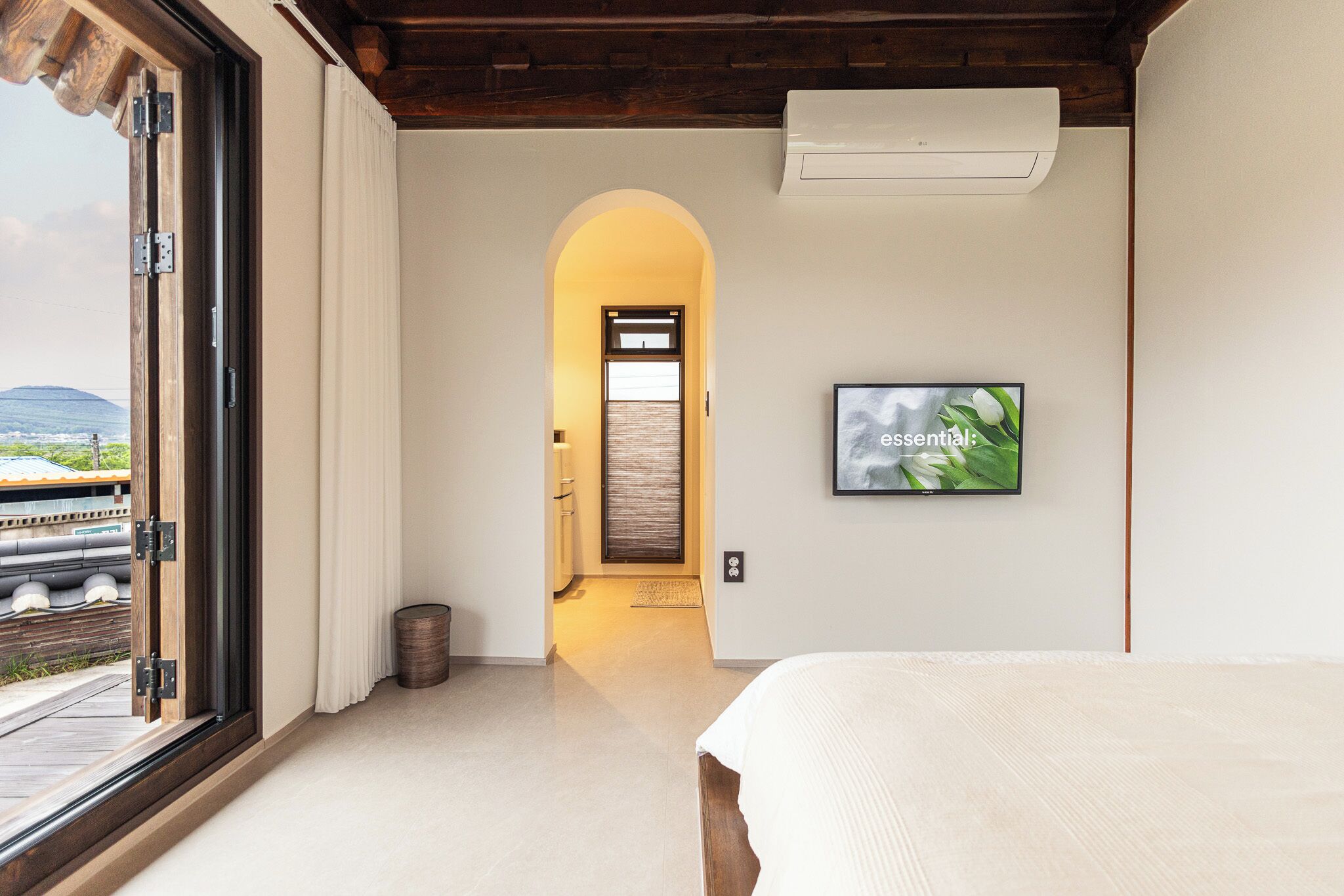 Ein Schlafzimmer mit großem Fenster, einem Bett, einem Fernseher und einer bogenförmigen Tür, die in einen anderen Raum führt.