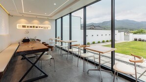 A modern dining area with a long table, chairs, and large windows offering a view of traditional architecture and mountains. - Hwarangroo (Gyeongju)