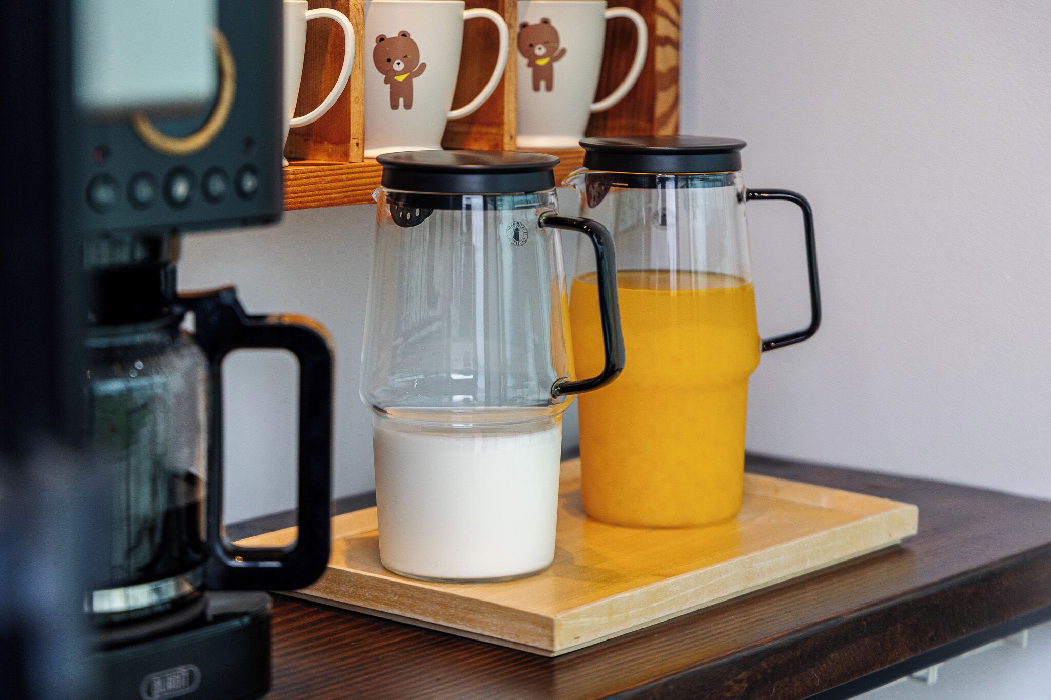 A coffee maker, two glass carafes, and a jug of orange juice on a wooden tray.