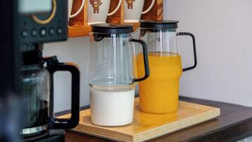A coffee maker, two glass carafes, and a jug of orange juice on a wooden tray.