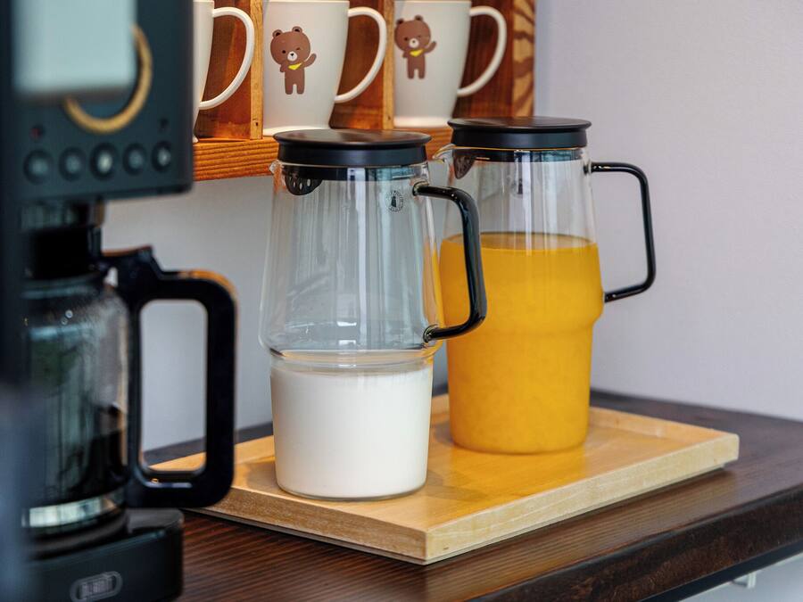 A coffee maker, two glass carafes, and a jug of orange juice on a wooden tray.