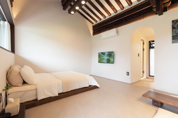 Un dormitorio con una cama, un banco, un aire acondicionado de pared y una puerta que da a otra habitación.