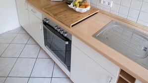 Cocina compacta con microondas, tostadora, hervidor y tabla de cortar con frutas.