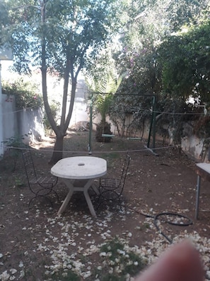 An outdoor seating area with a round table and chairs, surrounded by trees and a fence.