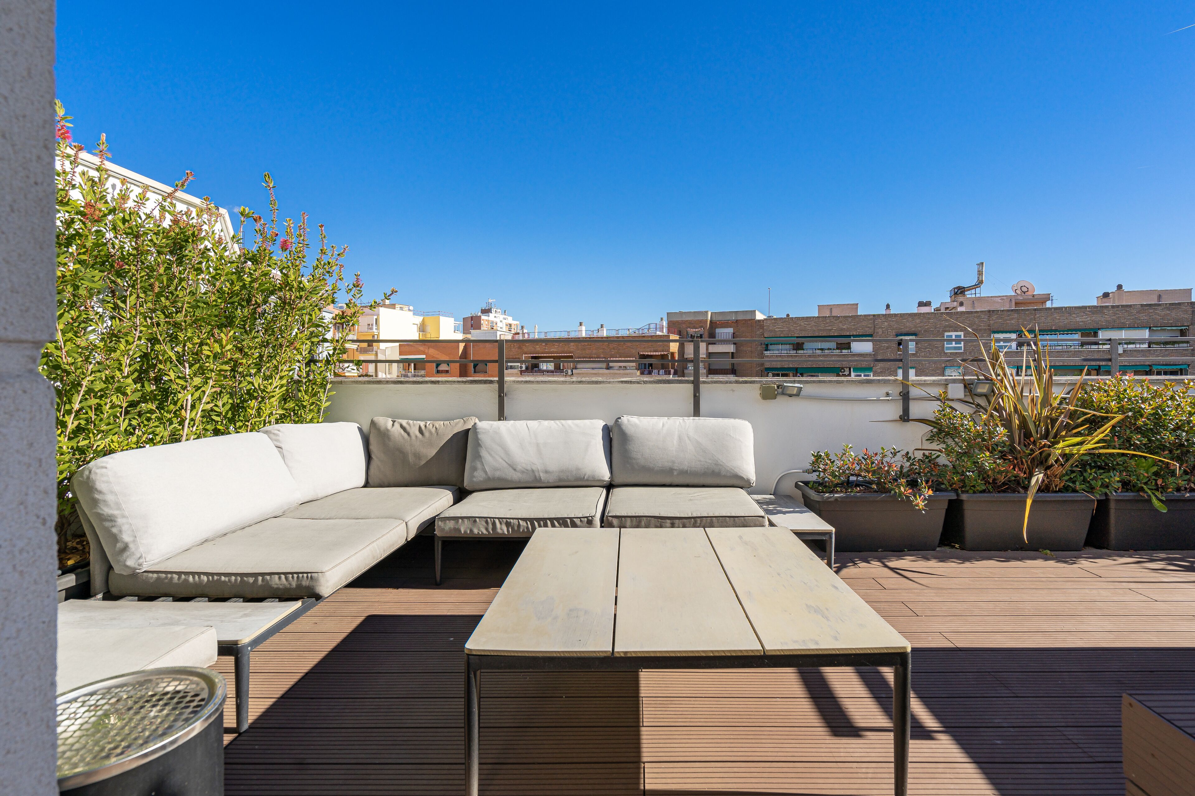 Eine Dachterrasse mit einer Eckcouch, einem kleinen Tisch und Topfpflanzen.