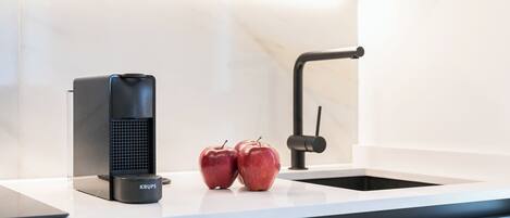 A kitchen counter with a coffee maker, two apples, and a sink.