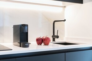 A kitchen counter with a coffee maker, two apples, and a sink.