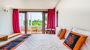 Ein Hotelzimmer mit einem großen Bett, einem Balkon mit roten Vorhängen und Blick auf Grünflächen.