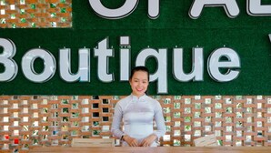 Eine Person steht hinter einem Empfangstresen, im Hintergrund ist eine Schilderung mit dem Wort 'Boutique' zu sehen.