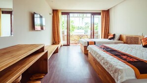 Ein Hotelzimmer mit Holzschreibtisch, zwei Betten, einem Fernseher und einem Balkon mit Vorhängen.