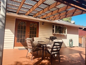 A covered patio with a table and chairs, a grill, and a hose coiled against the wall. - The Gathering Place 3BR + Game Room (Keizer)