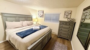 A bedroom with a bed, dresser, nightstand, lamp, and artwork.