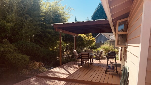 Puuinen terassi, jossa on ulkokalusteita, grilli ja pergola.