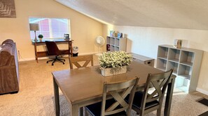 A dining area with a wooden table, chairs, a potted plant, and a bookshelf.