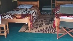 A tented accommodation with two beds, a small table, and a foldable chair.