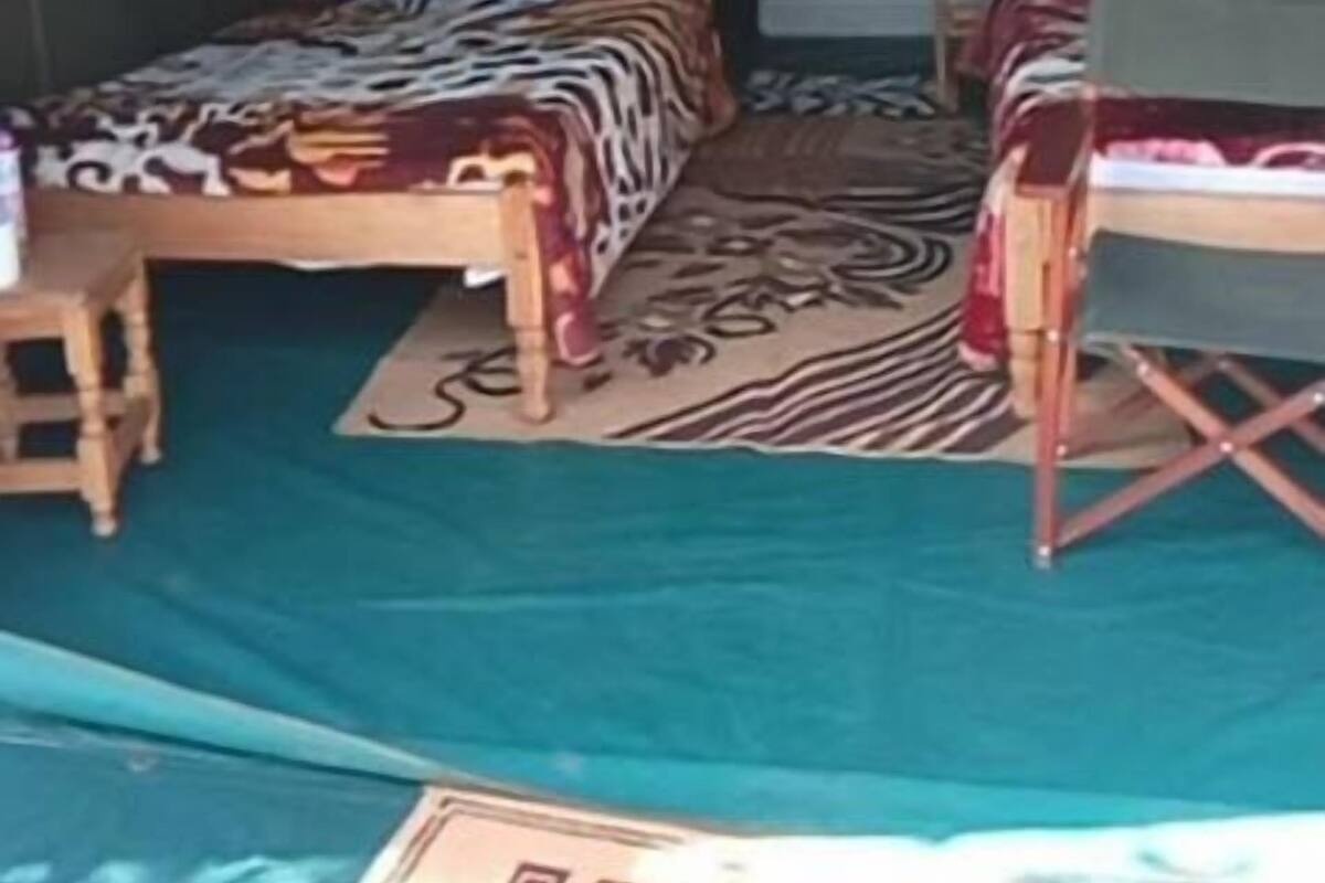 A tented accommodation with two beds, a small table, and a foldable chair.