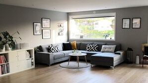 A modern living room with a grey sofa set, a coffee table, and a dining area with a white table and chairs. - Solferie Justnesskauen 21 (Kristiansand)