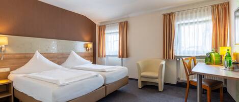 A hotel room with two beds, a desk, a chair, and a lamp.