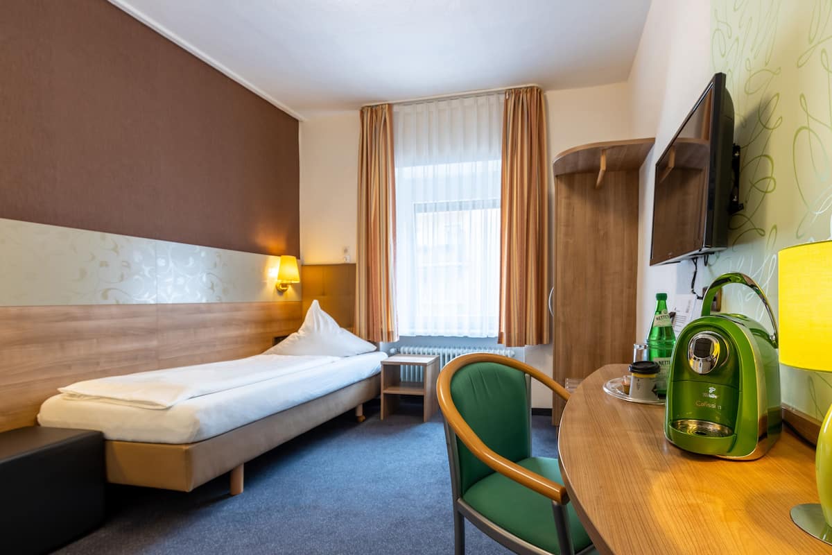 Habitación de hotel con cama, sillón, mesita, cafetera y televisor montado en la pared.
