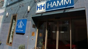 Entrada de hotel con un llamativo letrero 'HH HAMM' y un letrero 'HOTEL HAMM' debajo.