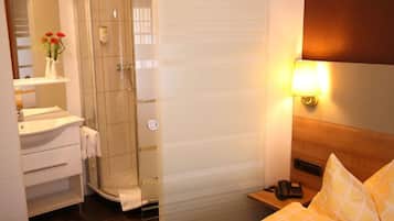 A hotel room with a shower, a bedside table with a lamp, a phone, and a bed with a checkered pillow.