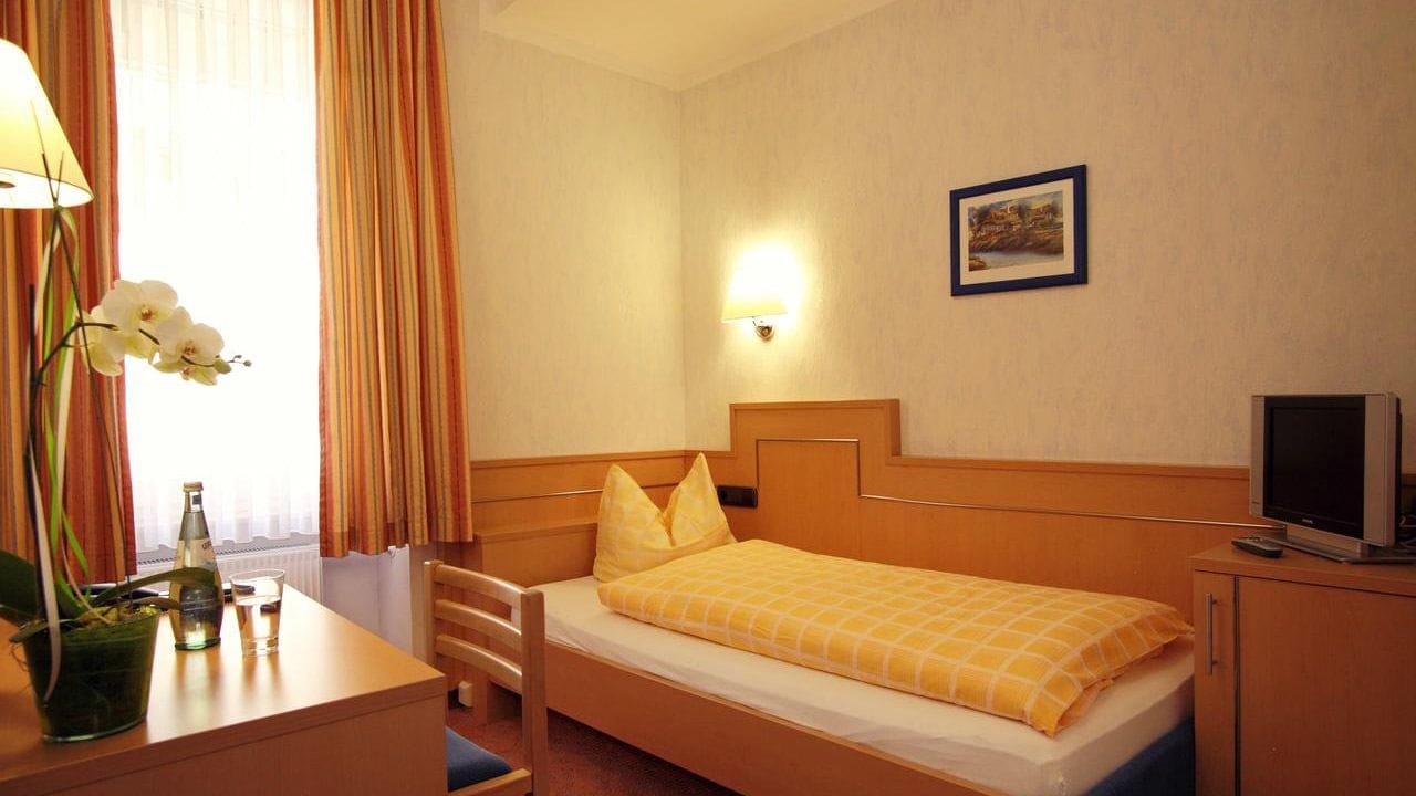 A hotel room with a bed, a desk with a lamp, a television, and a picture on the wall.