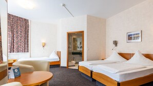 A hotel room with two single beds, a small table, a chair, a desk, a bathroom with a glass door, and a window with curtains. - Trip Inn City Hotel Hamm Koblenz (Koblenz)