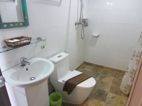 A bathroom with a white sink, toilet, and shower. There is a green trash bin and a basket on the wall.