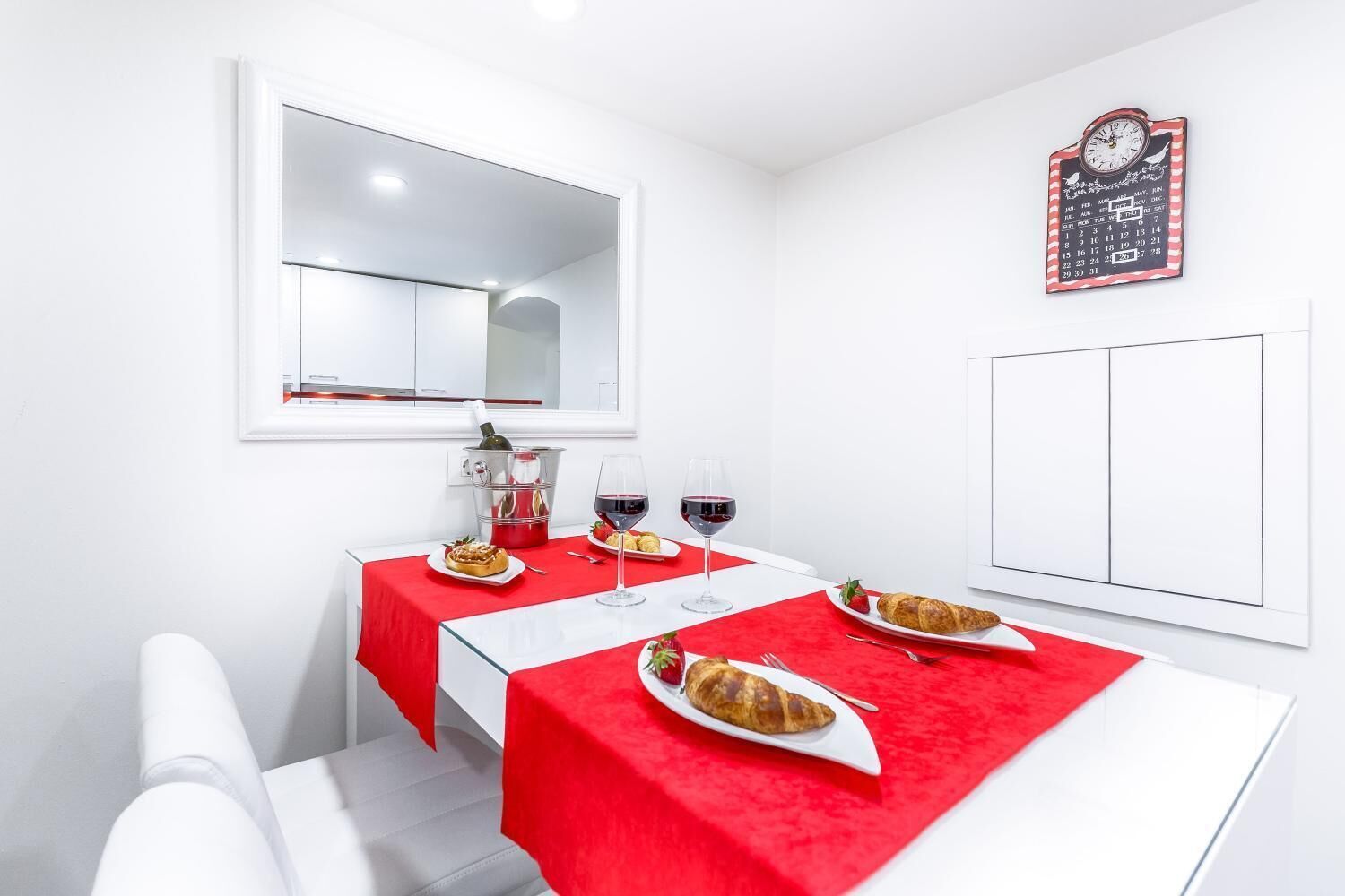 Een kleine, moderne kamer met een eettafel gedekt voor twee personen, een fles wijn, glazen en een croissant.