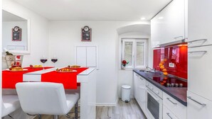 A compact kitchen with white cabinets, a red countertop, and a small window. - Fiorello Apartment (Rijeka)