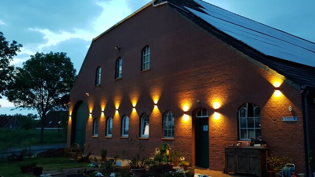 A brick building with multiple windows and a sloped roof, illuminated by exterior lights. - Apartment "Dat Nüst", terrace, garden, mod. bath (Manslagt)